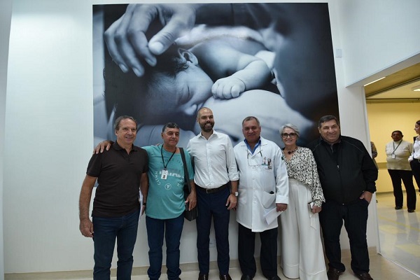 #PraCegoVer: Na foto, o secretário municipal da saúde Edson Aparecido e o prefeito Bruno Covas posam durante a inauguração da sala de parto humanizado. Ao fundo, há uma fotografia de uma mulher segurando um bebê, estampada na parede da sala. 